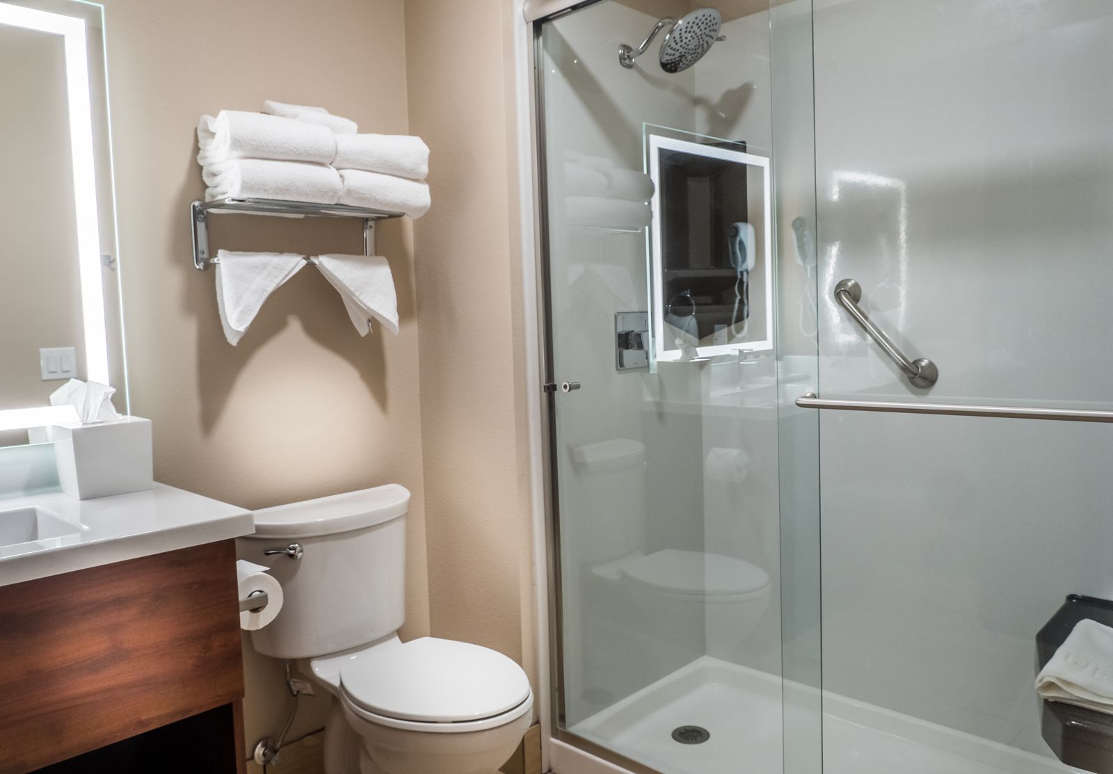 Un baño con inodoro, lavamanos, ducha con mampara de vidrio y toallero con toallas dobladas.