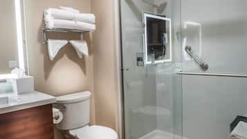 Un baño con inodoro, lavamanos, ducha con mampara de vidrio y toallero con toallas dobladas.