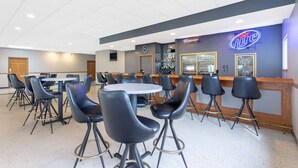 Zona de bar con varias mesas y sillas, una barra con letrero de neón y una exhibición de botellas de licor.