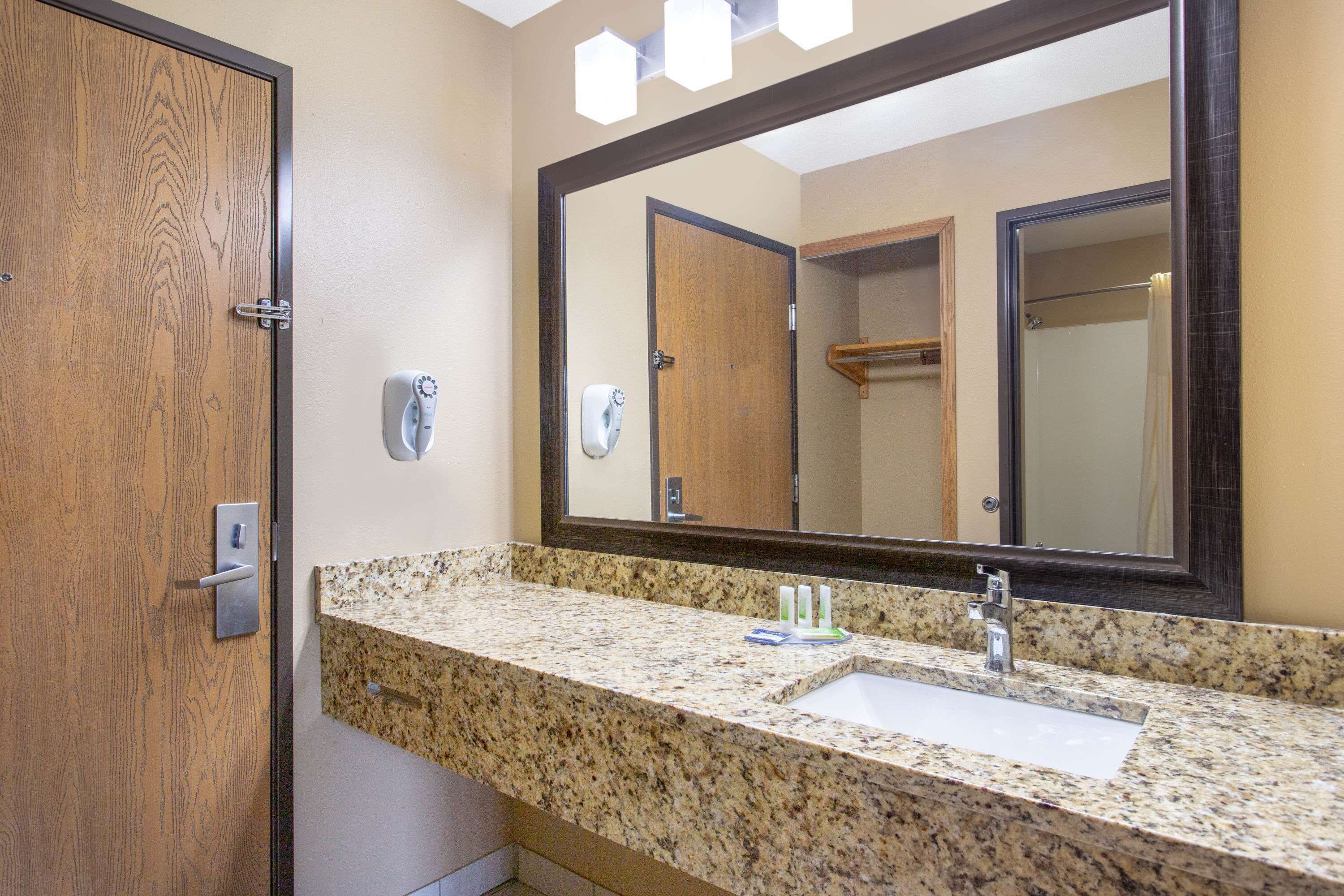 A bathroom with a granite countertop, a sink, a mirror, and a wooden door.