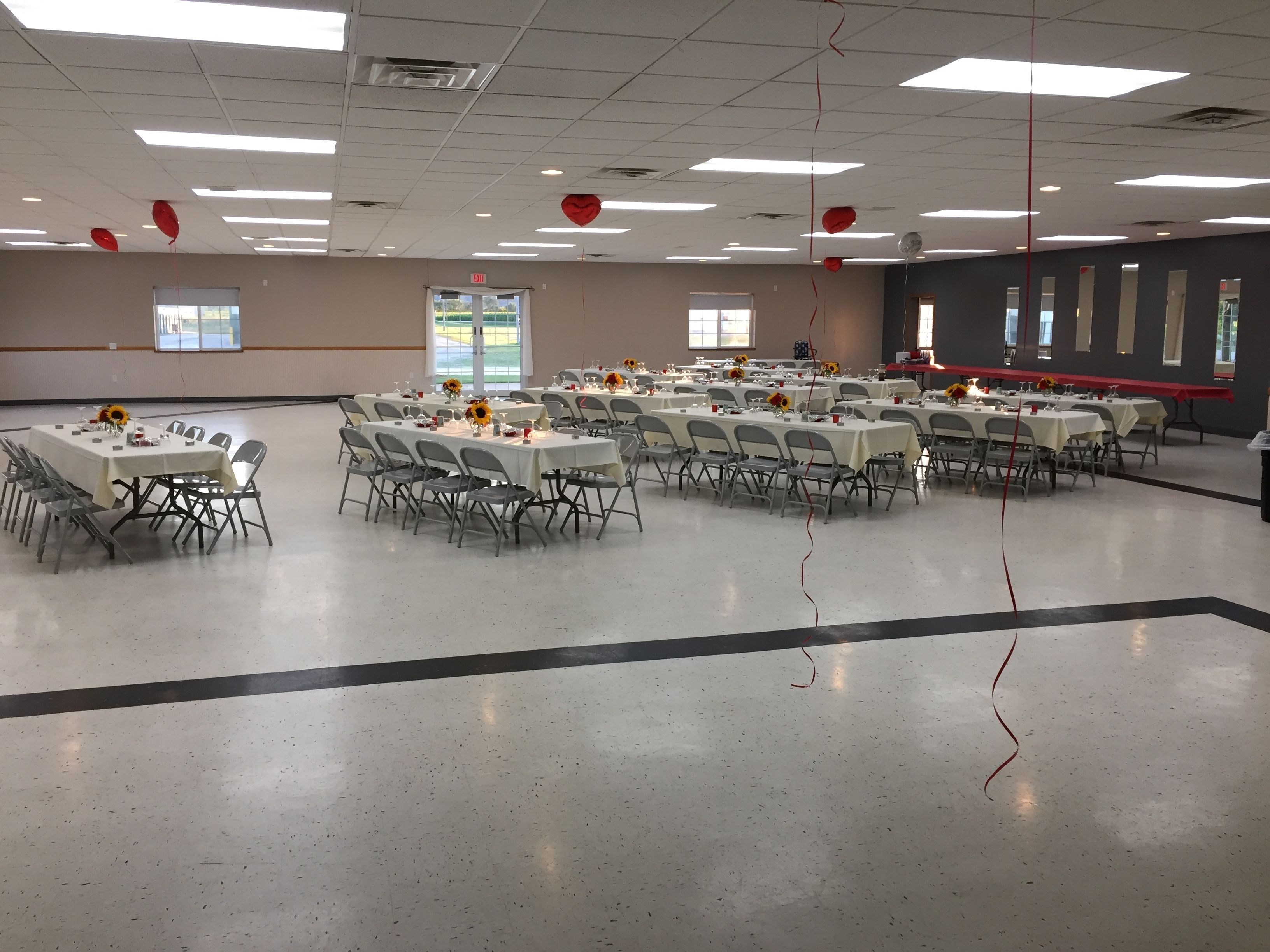 A large, well-lit hall with multiple tables set for dining, arranged in rows.