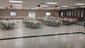 A large, well-lit hall with multiple tables set for dining, arranged in rows.