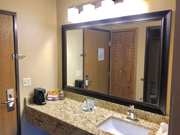 A bathroom with a large mirror, granite countertop, sink, and a coffee maker. - AmericInn by Wyndham Boscobel (Boscobel)
