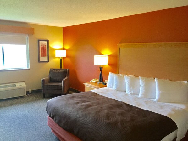 A hotel room with a large bed, two bedside lamps, a chair, and a window.