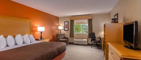 A hotel room with a large bed, two bedside lamps, a television on a wooden cabinet, a chair, and a window with curtains.