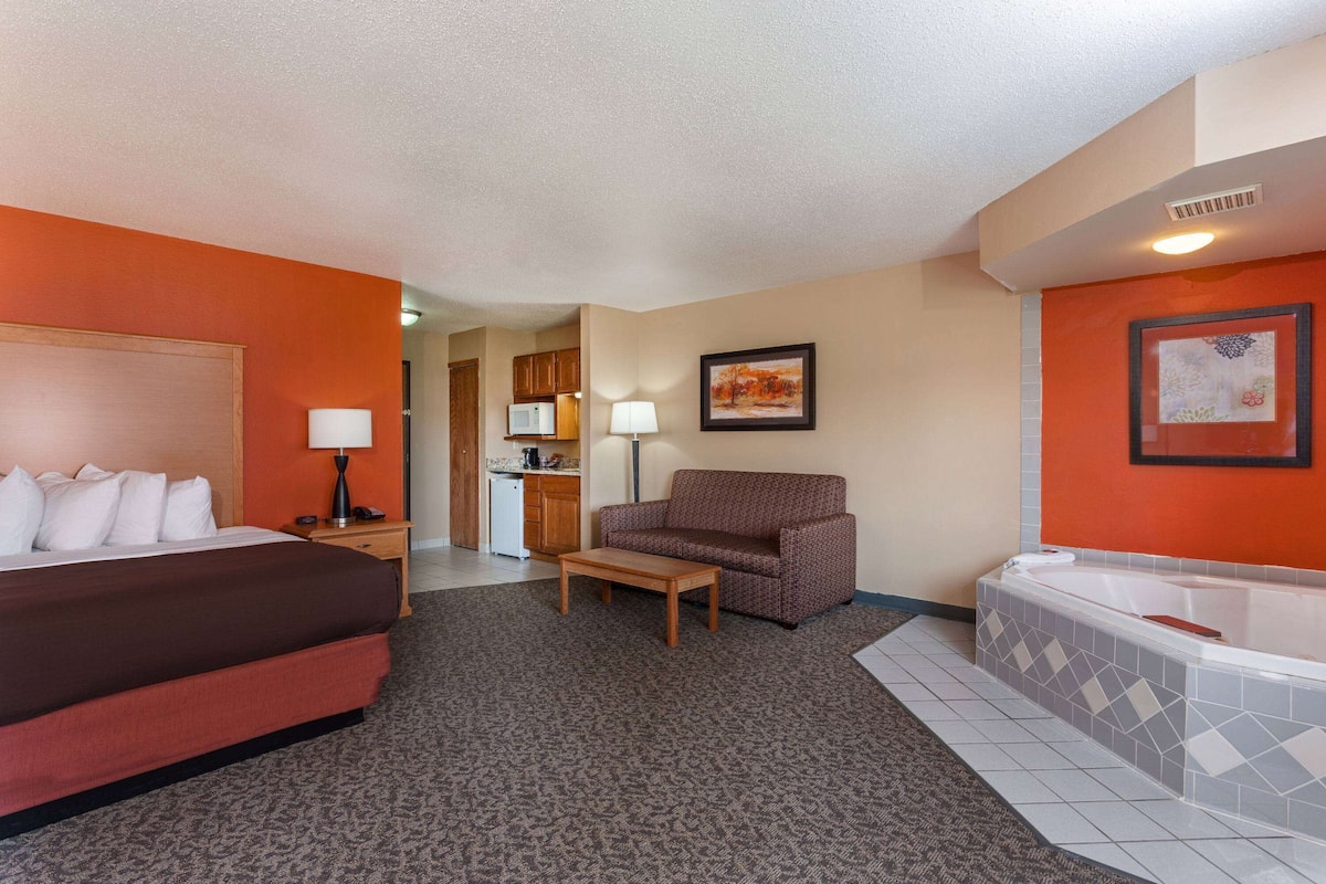 A hotel room with a bed, a sofa, a small table, a kitchenette, and a bathtub.