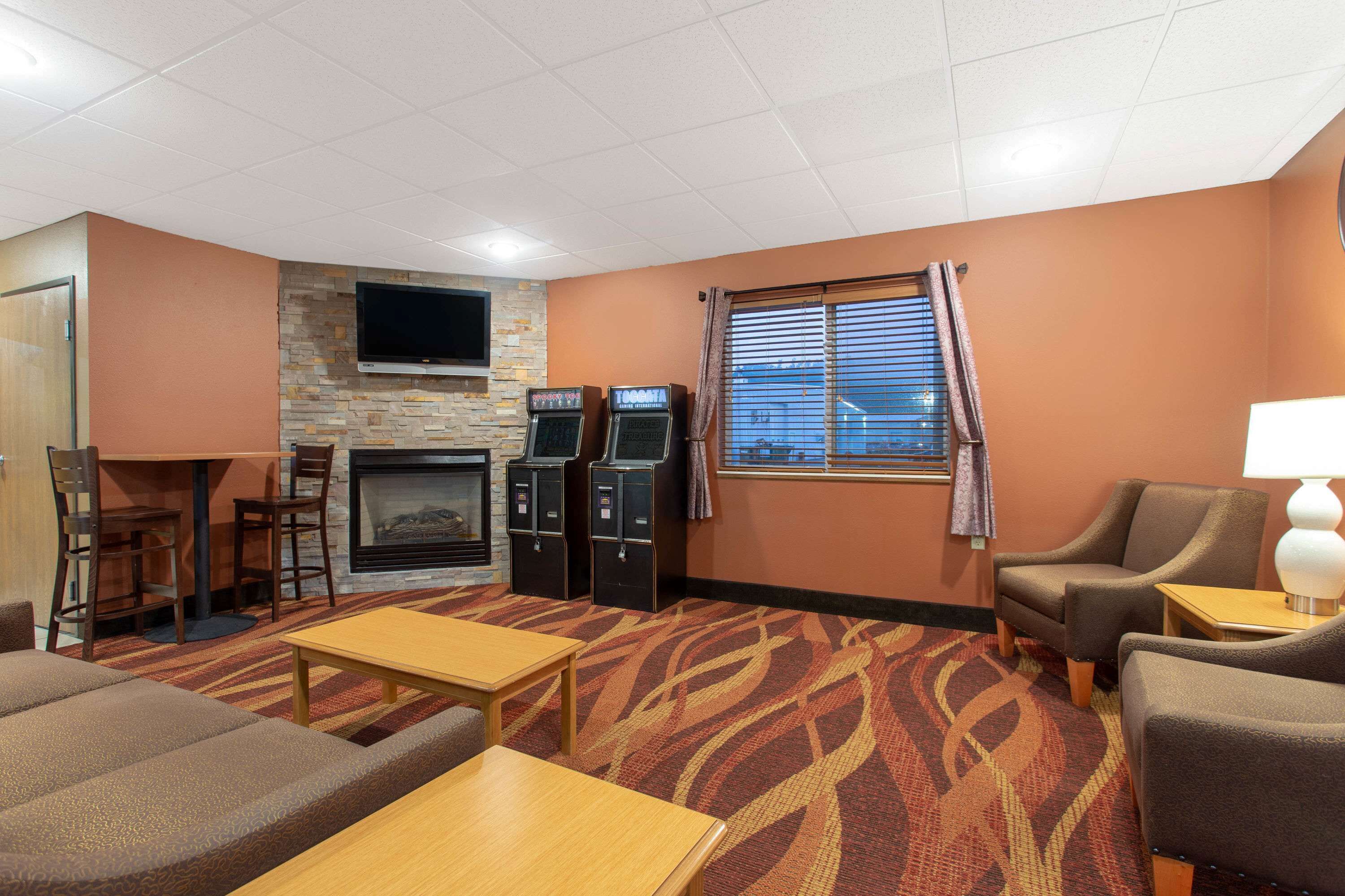 A hotel room with a fireplace, a flat-screen TV mounted on the wall, a carpeted floor, and a seating area with a sofa and armchairs.