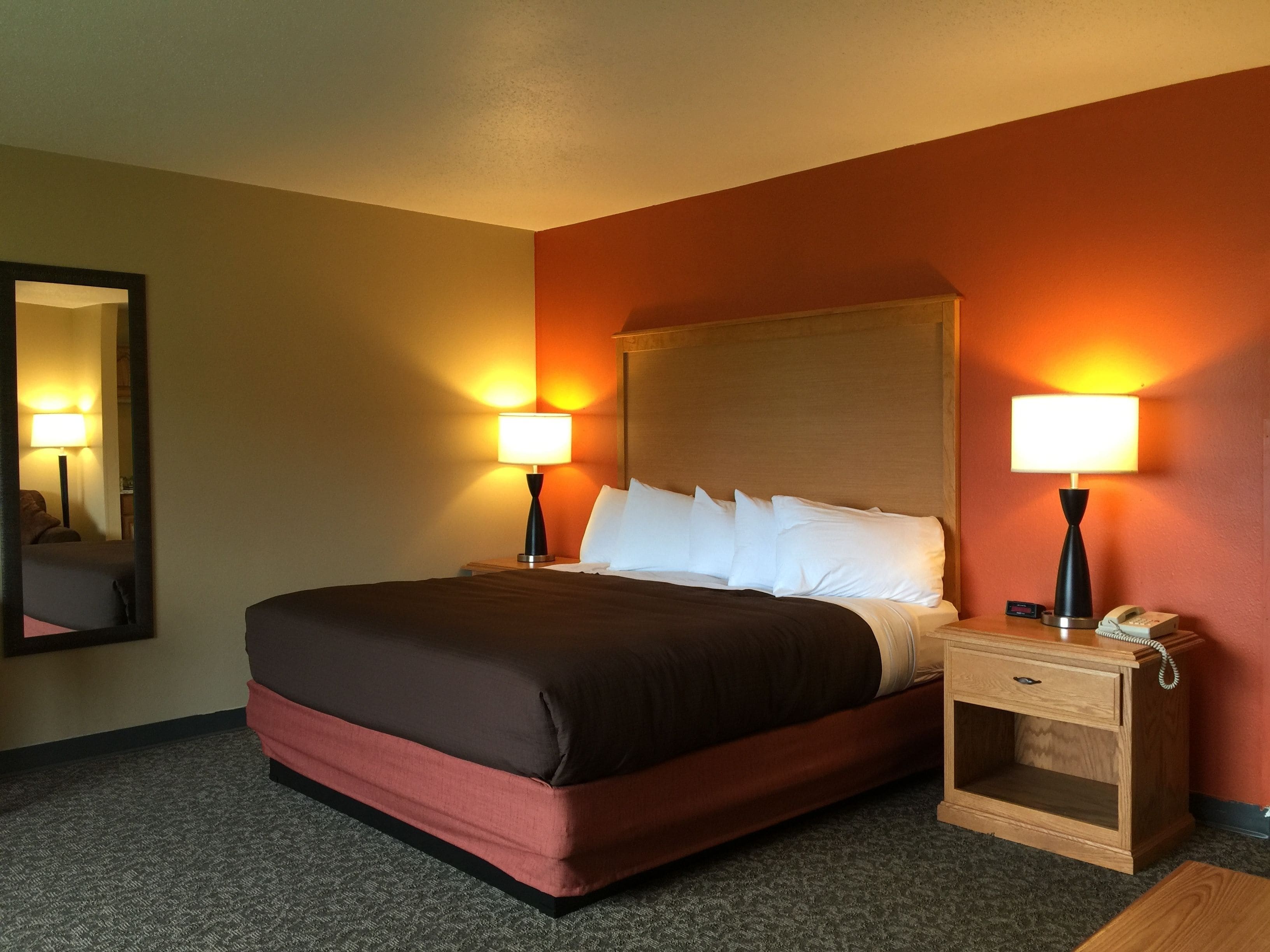 A hotel room with a large bed, two bedside lamps, a nightstand with a phone, and a mirror on the wall.