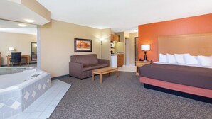 Habitación de hotel con una cama grande, un sofá, una mesita, un escritorio, una silla, una lámpara, un cuadro y un baño con bañera.