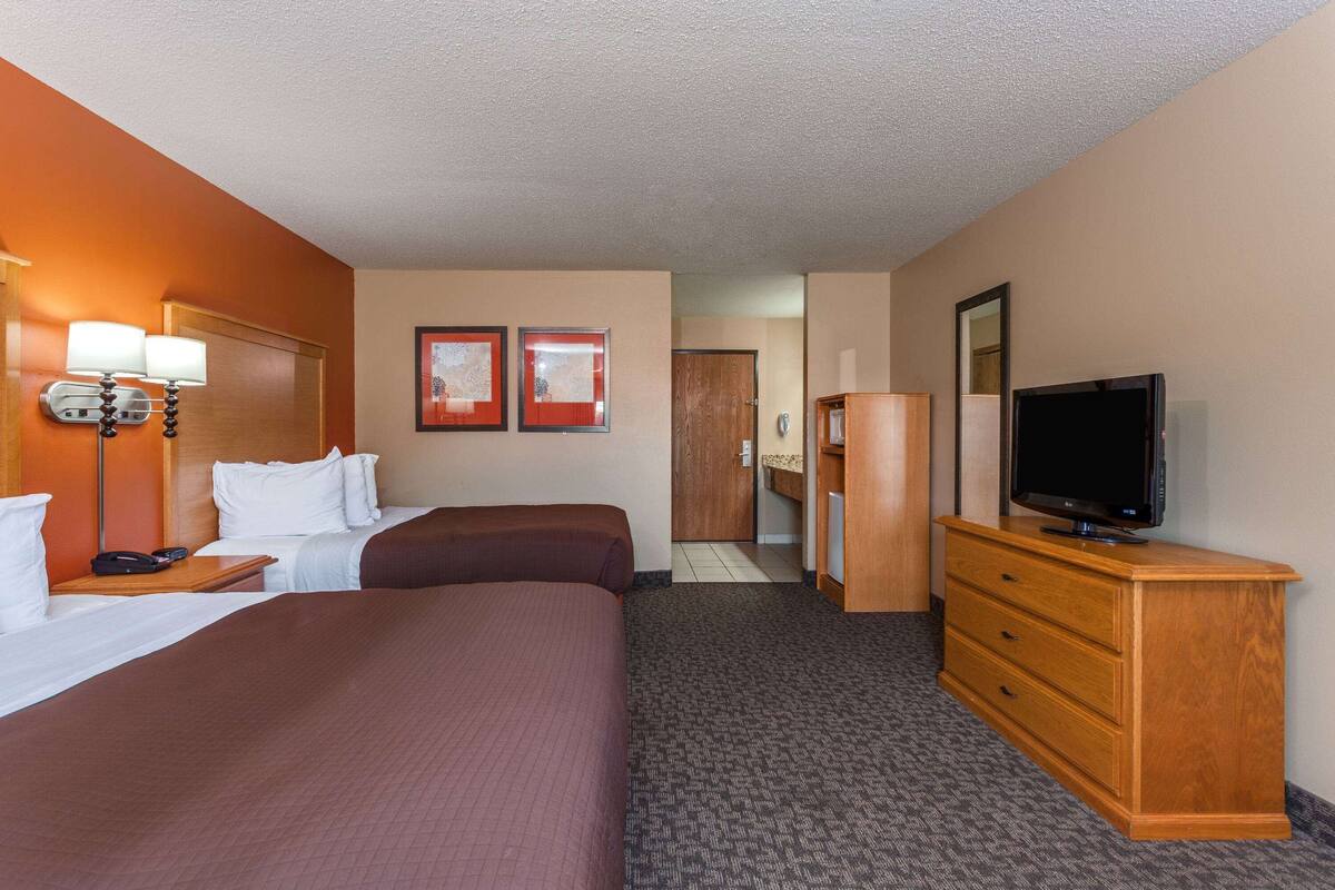 A hotel room with two beds, a wooden dresser, a television, and a desk with a lamp.