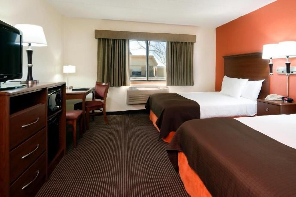 A hotel room with two beds, a desk, a chair, a TV, and a window with curtains.