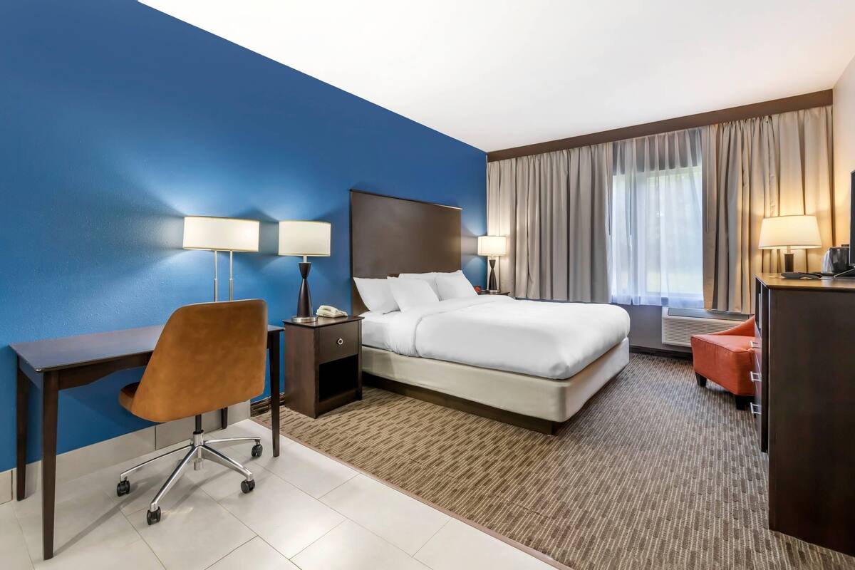 A hotel room with a bed, desk, chair, and two lamps.
