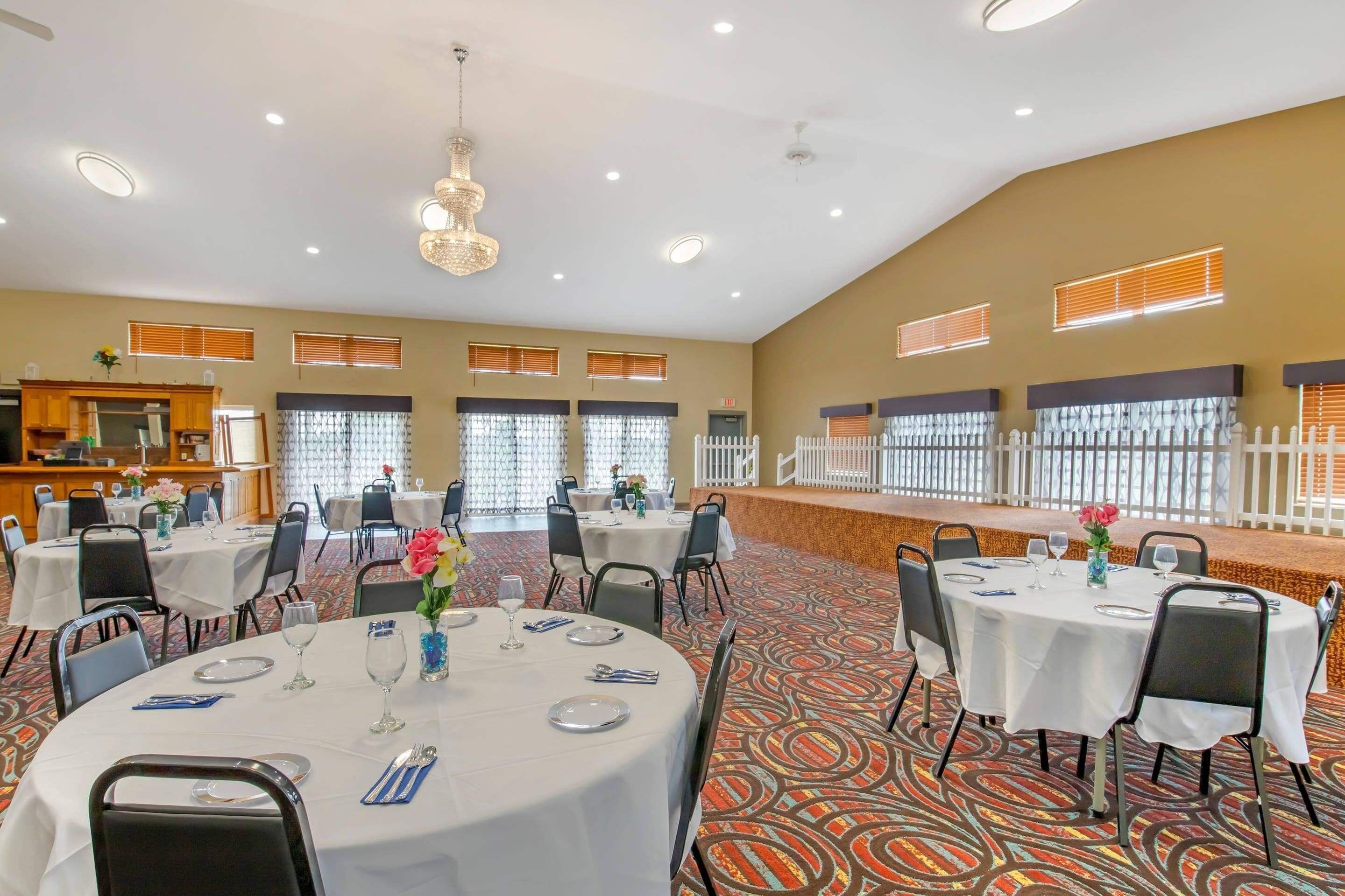 Un amplio salón de banquetes con varias mesas redondas dispuestas para cenar, una zona de bar y una lámpara decorativa.