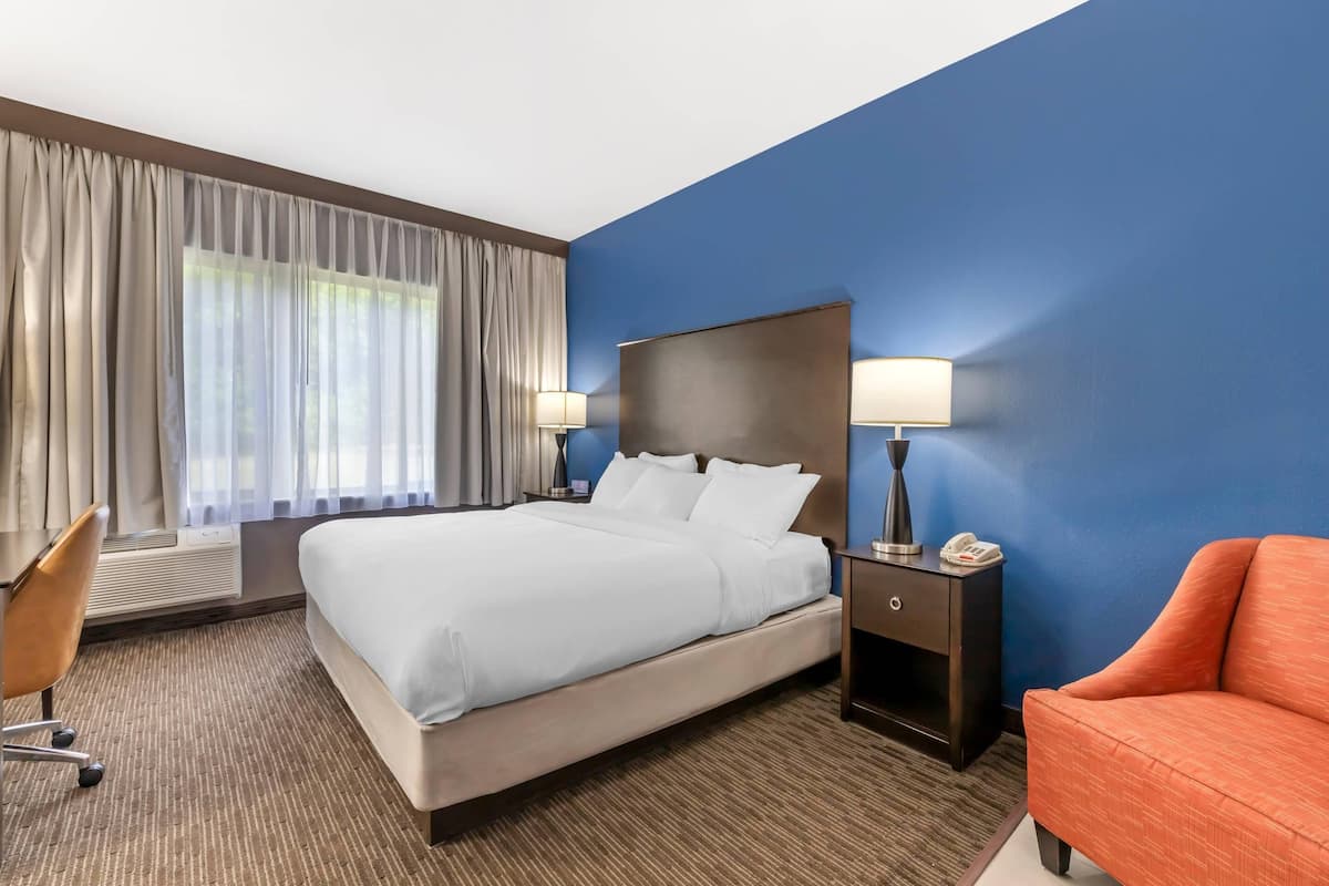 A hotel room with a bed, two bedside lamps, a desk with a chair, and a sofa.