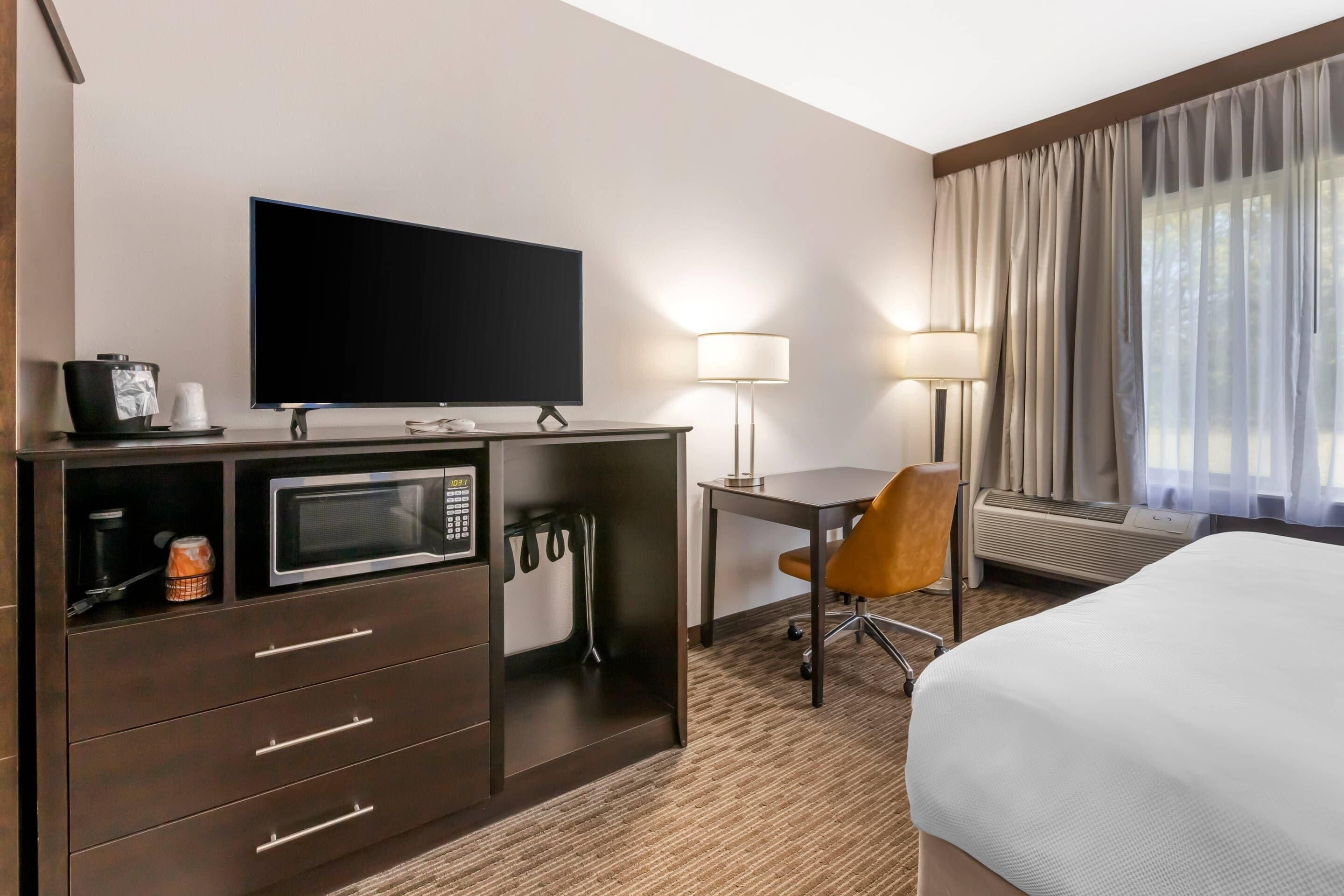 Habitación de hotel con televisión de pantalla plana, microondas, escritorio con silla, cama y ventana con cortinas.