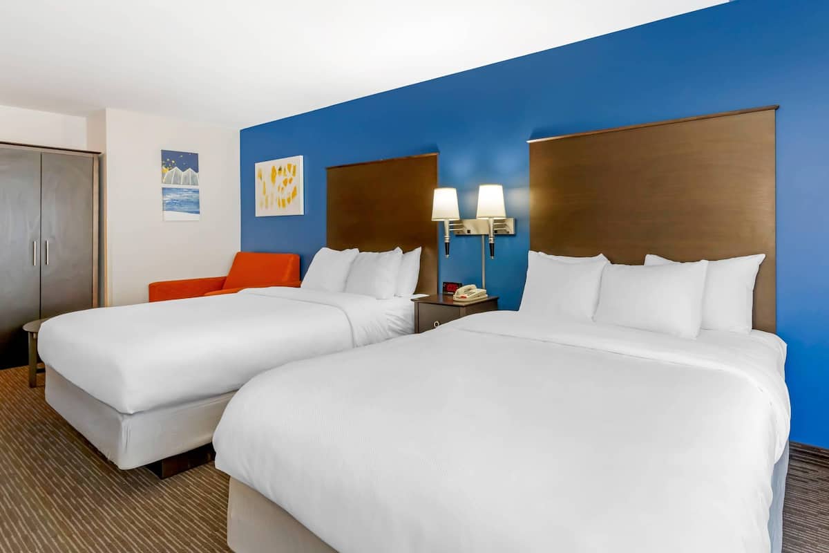 A hotel room with two beds, a nightstand, a phone, and artwork on the wall.