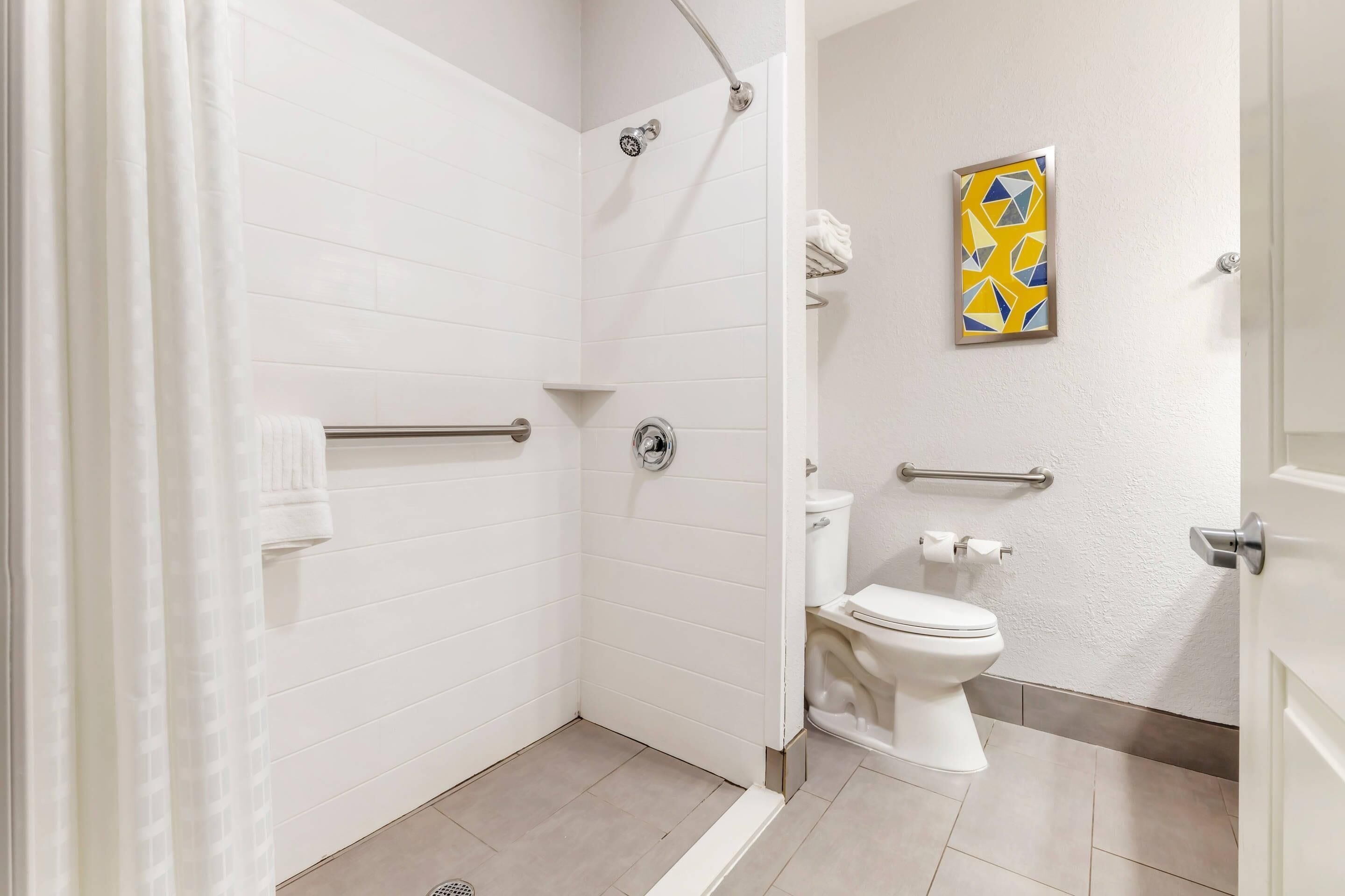 Un baño moderno con paredes de azulejos blancos, una ducha con puerta de vidrio, un inodoro y una barandilla.