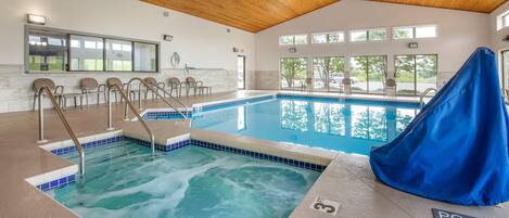 An indoor swimming pool with a wooden ceiling, clear windows, and a pool lift.