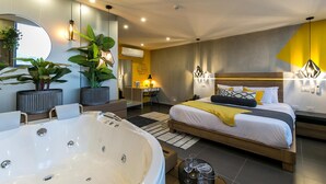 A modern bedroom with a large bathtub, a bed with yellow bedding, and a desk area. - Epic Hotel Boutique (Medellín)