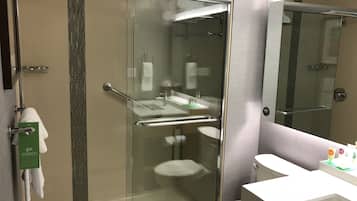 Un baño moderno con cabina de ducha de vidrio, inodoro blanco y tocador con espejo.