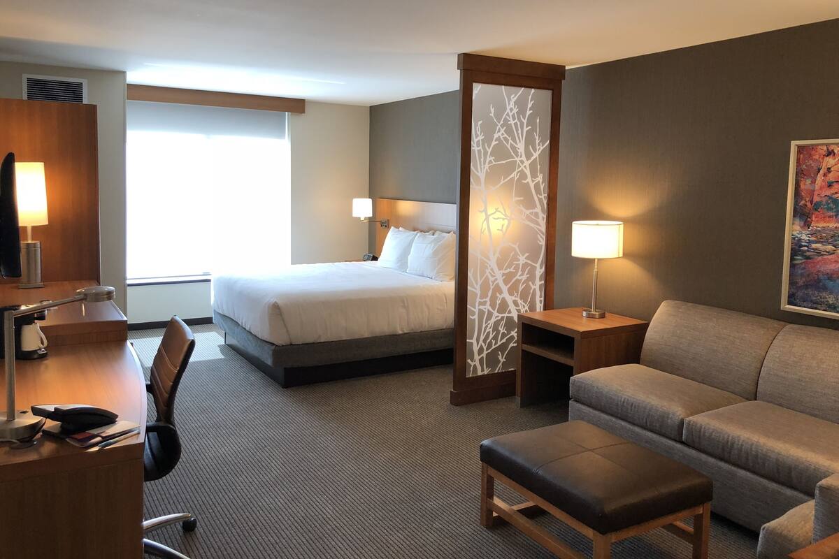A hotel room with a bed, a desk, a chair, a sofa, and a decorative wall panel.