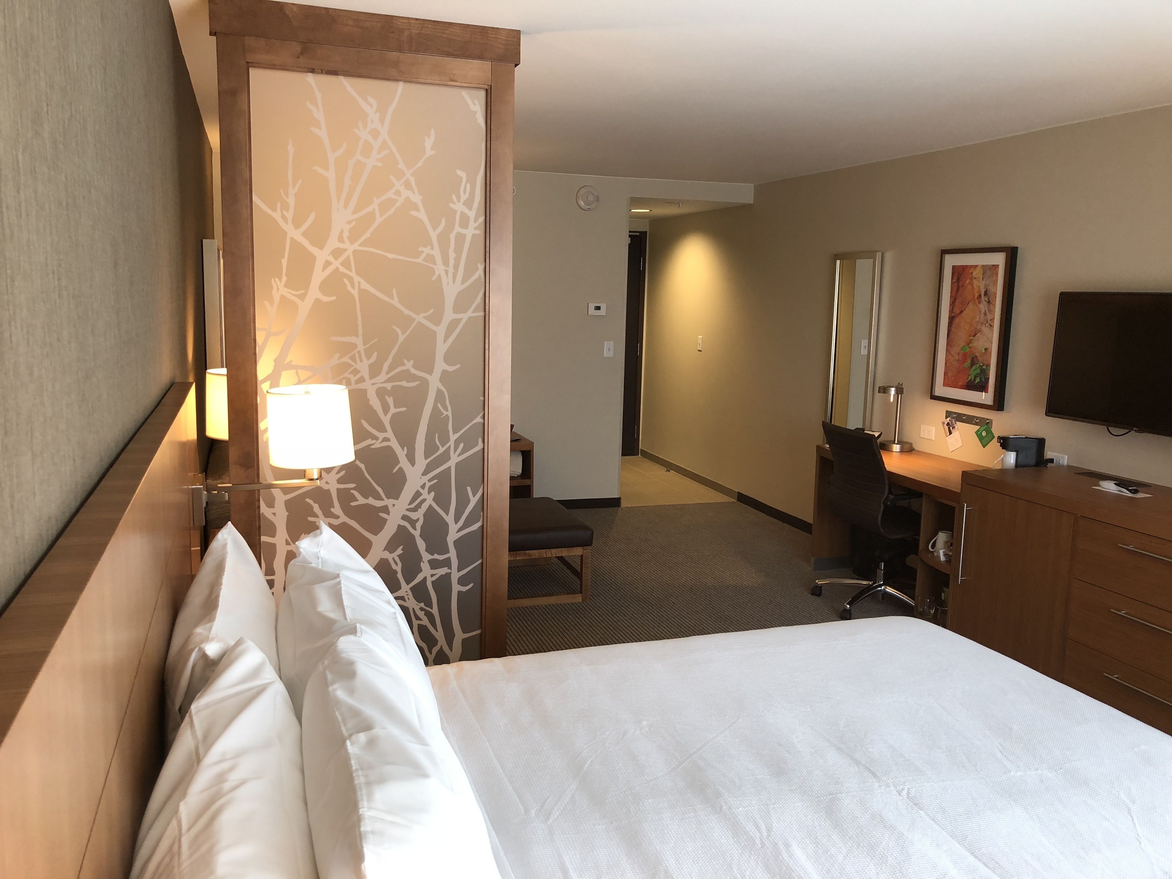 Una habitación de hotel con cama, escritorio, silla, televisor y lámpara.