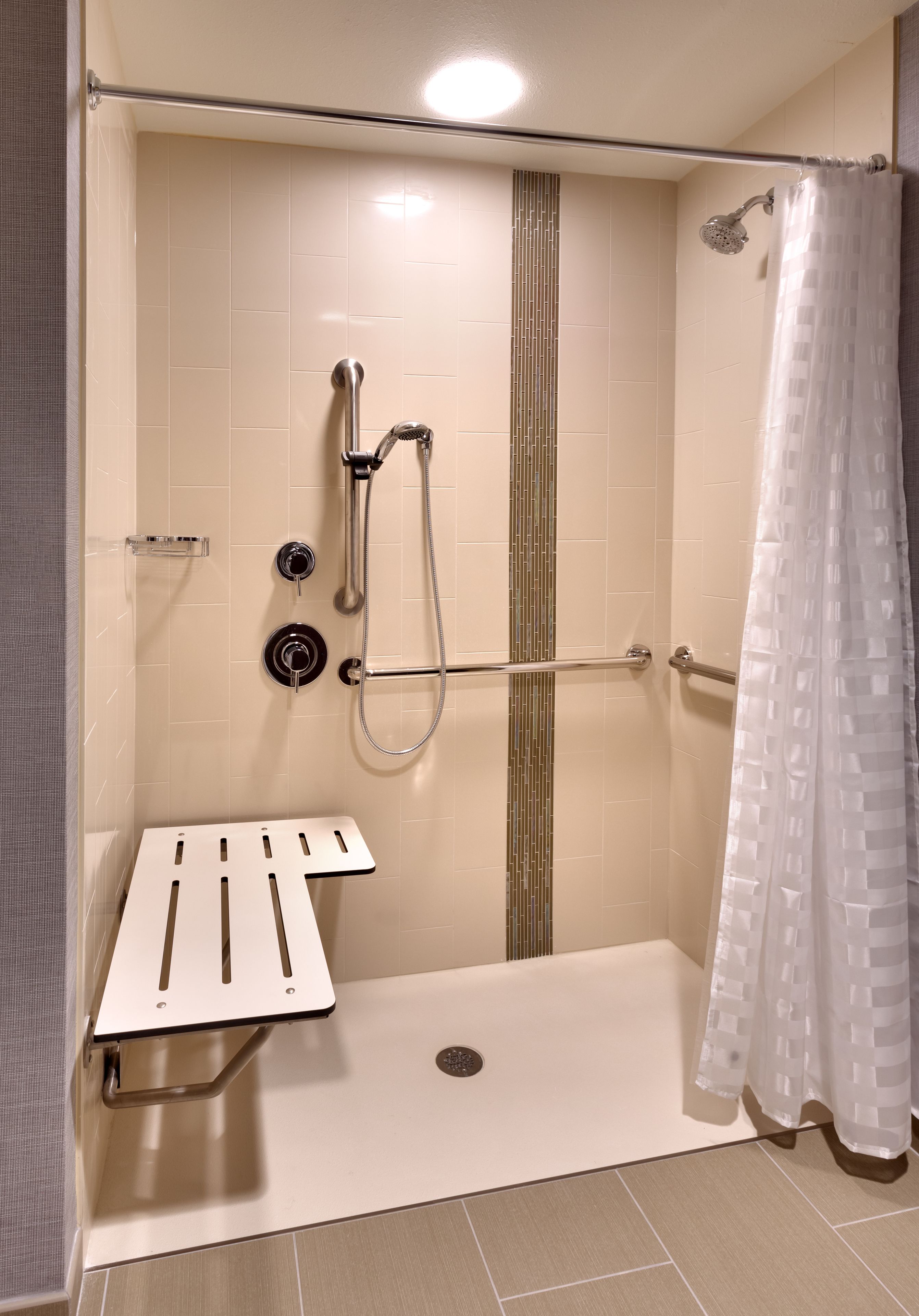 Een douche met lage drempel, een handgreep, een handdouche en een douchegordijn.