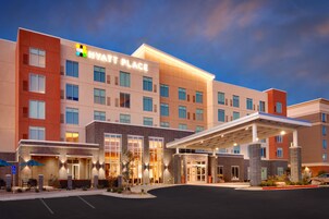 Un hotel moderno con un llamativo letrero de "HYATT PLACE", un acceso cubierto y un estacionamiento.