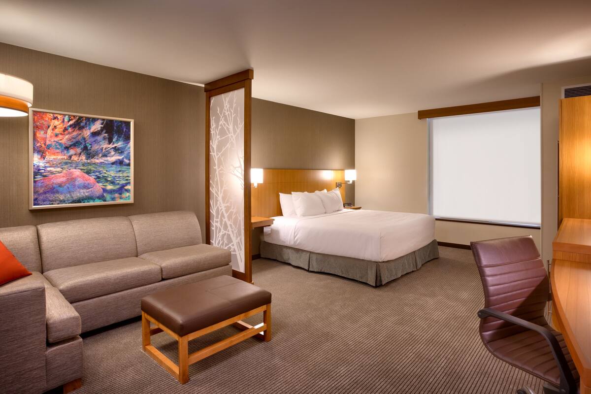 A hotel room with a bed, a sofa, a small table, a desk, and a projector screen.