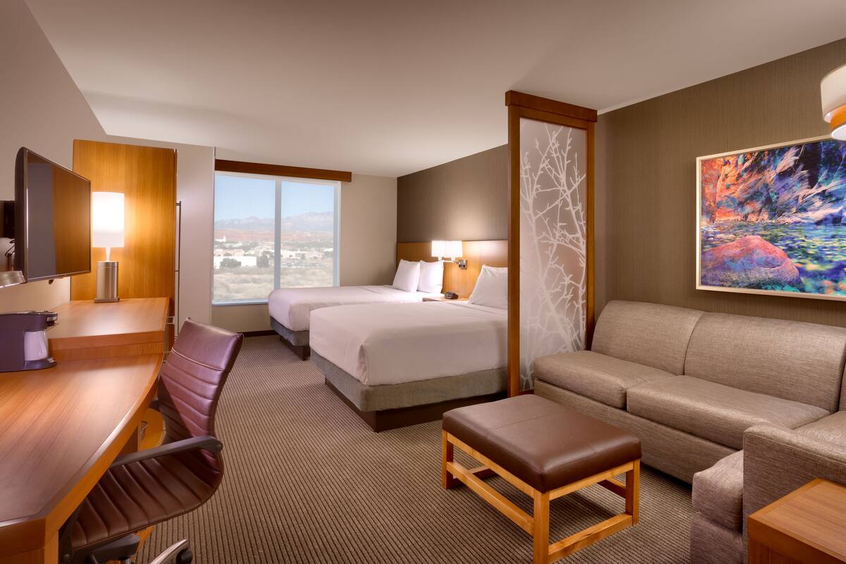 A hotel room with two beds, a desk, a chair, a sofa, and a painting.
