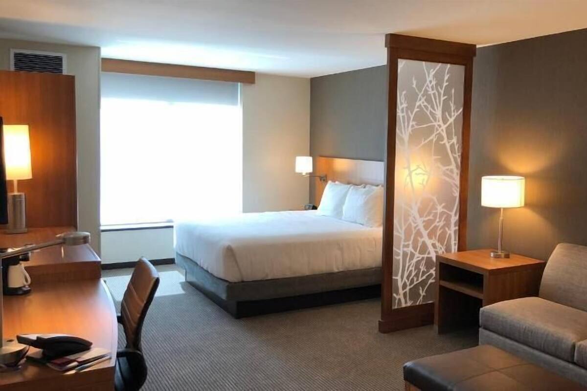 A hotel room with a bed, a desk, a sofa, and a painting on the wall.