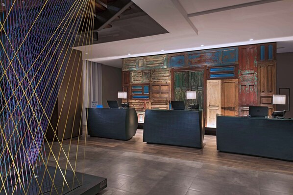 A modern reception area with three dark reception desks, a colorful abstract wall art, and a wooden panel wall with a rustic finish.