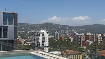 Une piscine sur le toit offrant une vue sur la ville, avec des bâtiments modernes et un ciel dégagé.