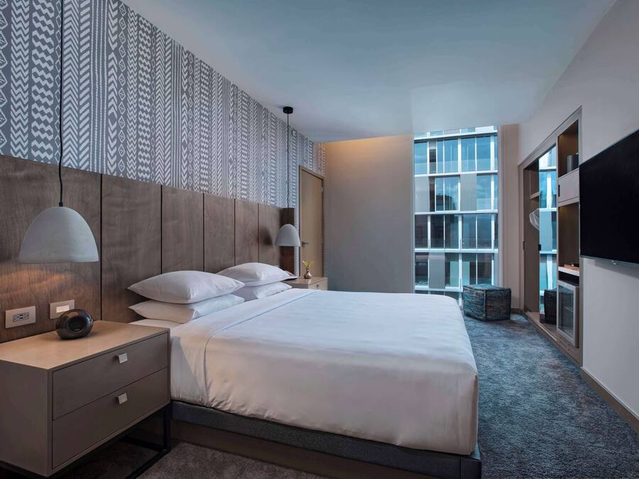 Ett modernt hotellrum med en stor säng, sänglampor, en platt-TV och en vägg med ett mönster.