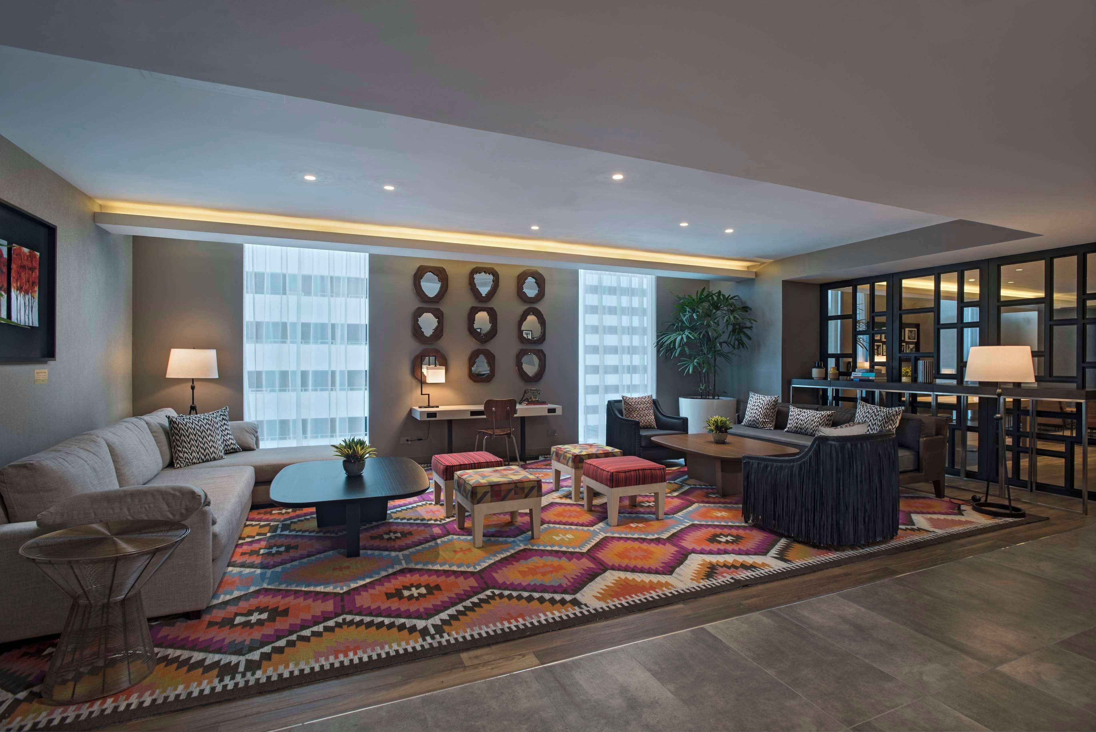 Un salon moderne comprenant un canapé, une table basse et des poufs, un tapis à motifs et un mur orné de miroirs décoratifs.