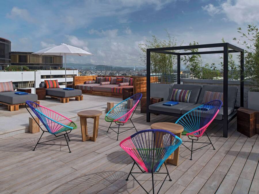 Une terrasse sur le toit, aménagée avec des coins salon, des chaises colorées et une pergola.