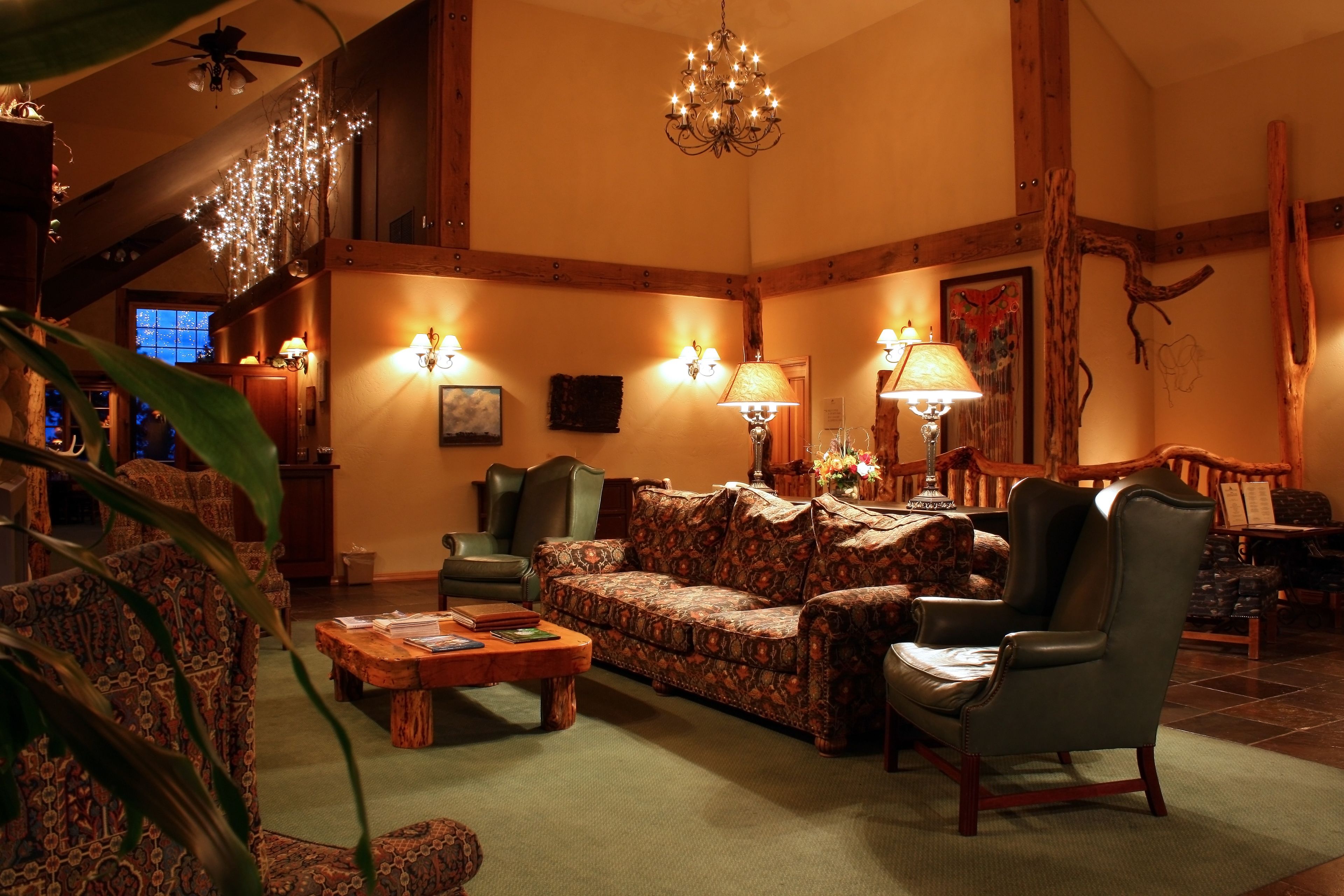 A cozy living room with a patterned sofa, a leather armchair, and a wooden coffee table. There are wall-mounted lamps and a chandelier.