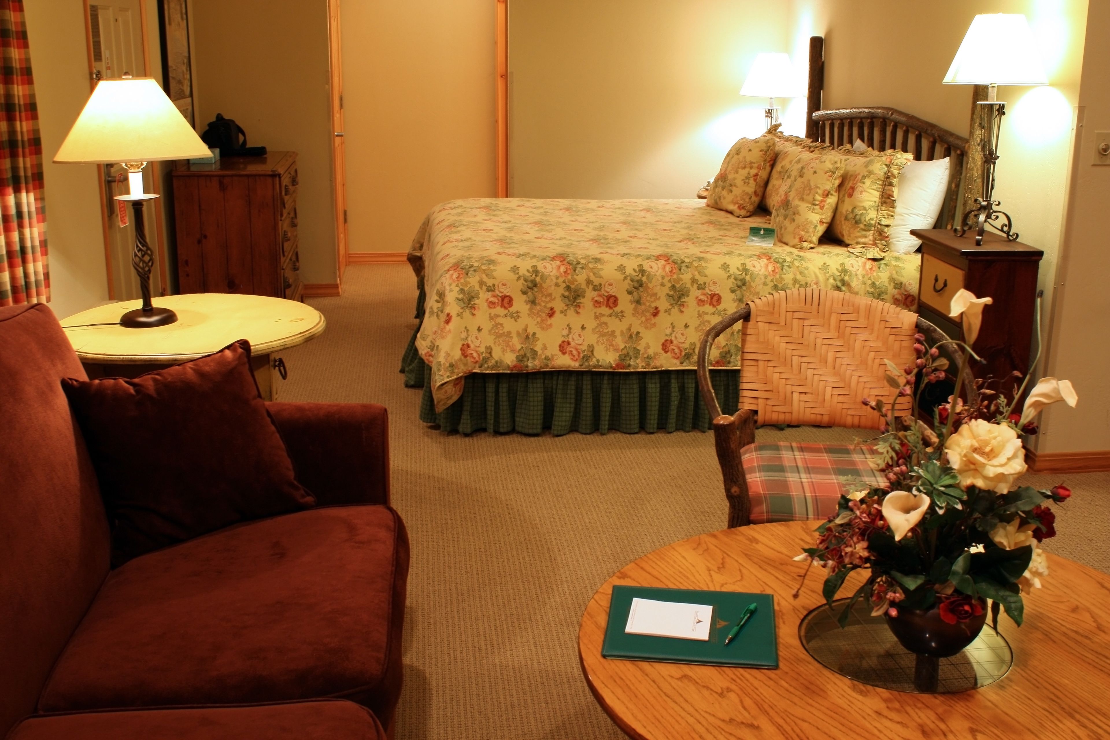 A hotel room with a bed, a desk, a chair, a table, and a vase of flowers.