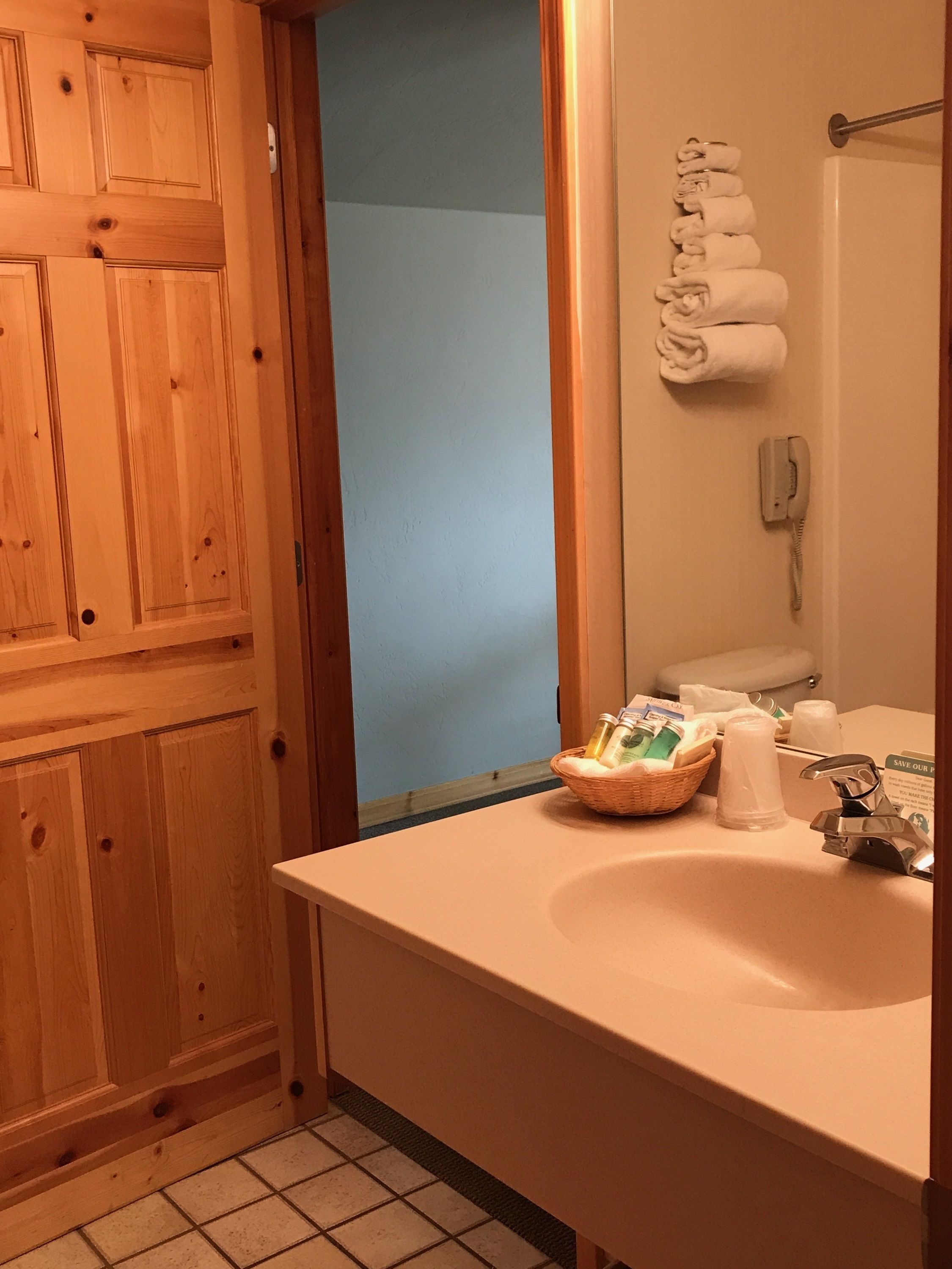 A bathroom with wooden paneling, a white sink, a mirror, a towel rack, a telephone, and toiletries on the counter.