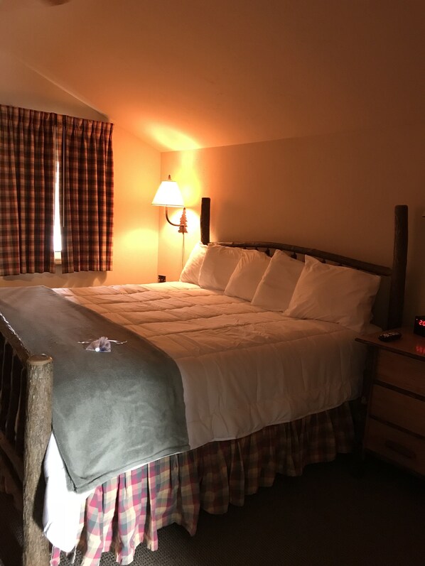 A neatly made bed with a plaid skirt, a bedside lamp, and a clock on the nightstand. - Mountain Lake Lodge (Bigfork)