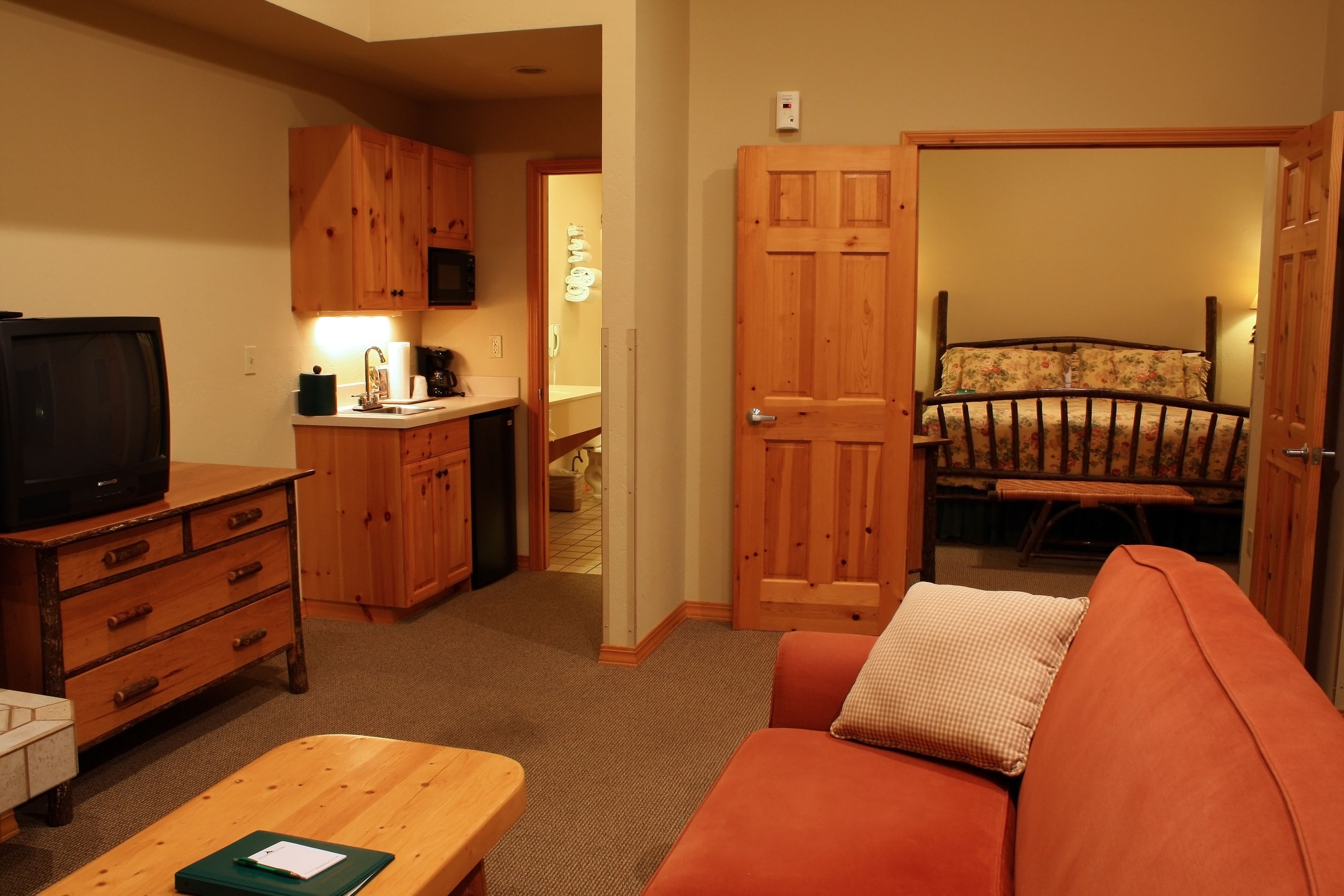 Een kleine kamer met een houten dressoir, een televisie, een bank en een bed met bloemenbedrukking.