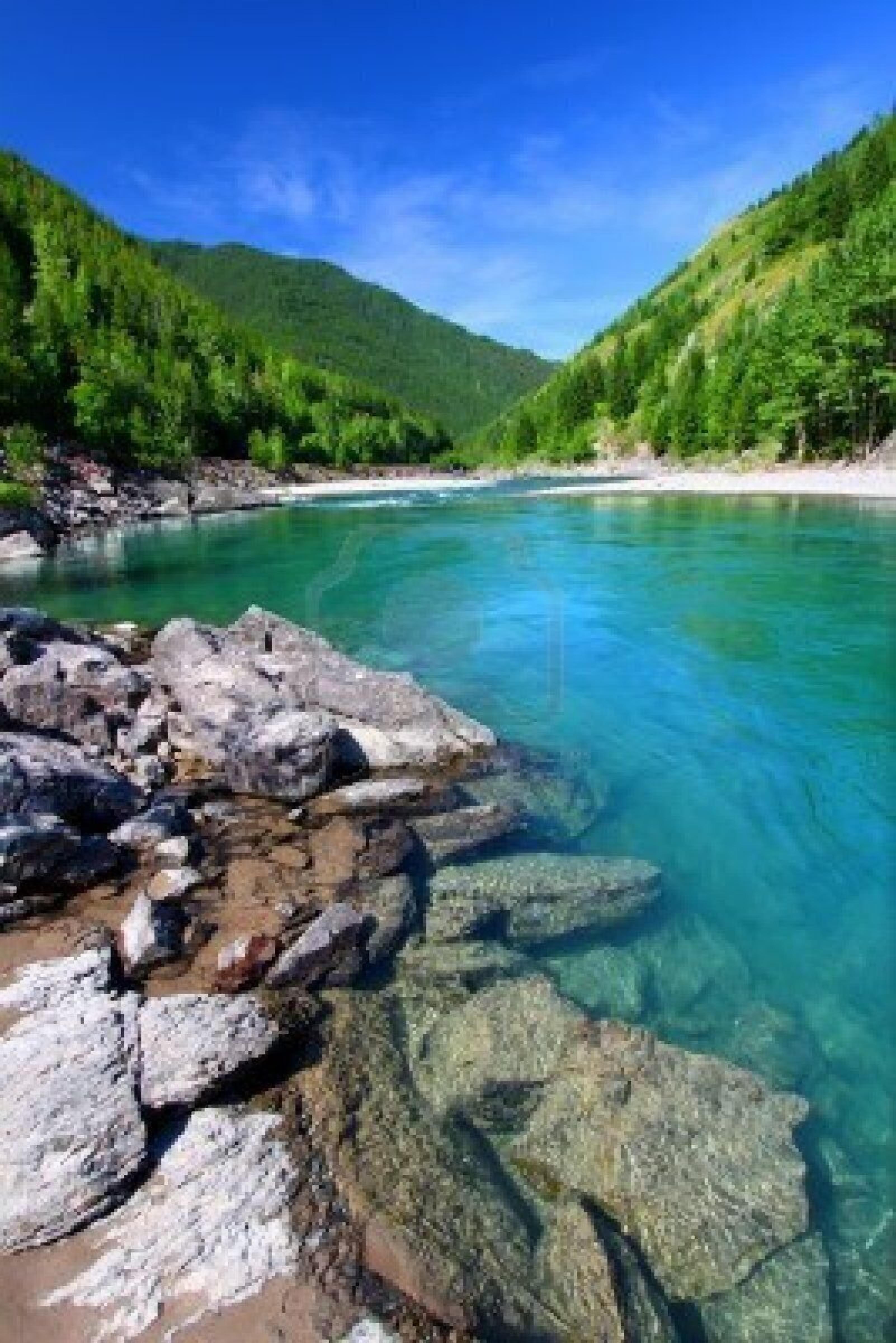 Une rivière aux eaux claires, avec des rochers au premier plan et des collines verdoyantes en arrière-plan.