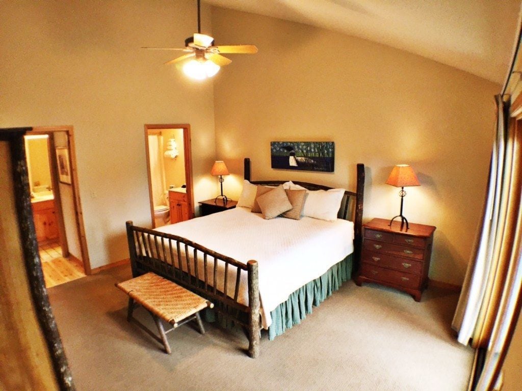 A bedroom with a single bed, bedside tables, a nightstand, a bench, a ceiling fan, and a painting on the wall.