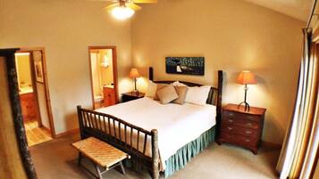 A bedroom with a single bed, bedside tables, a nightstand, a bench, a ceiling fan, and a painting on the wall.