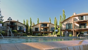 Un hotel con piscina, cascada, varios balcones y cielo despejado.