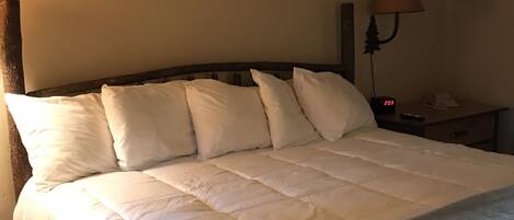 A neatly made bed with a wooden headboard, a bedside lamp, and a digital clock displaying 2:03.