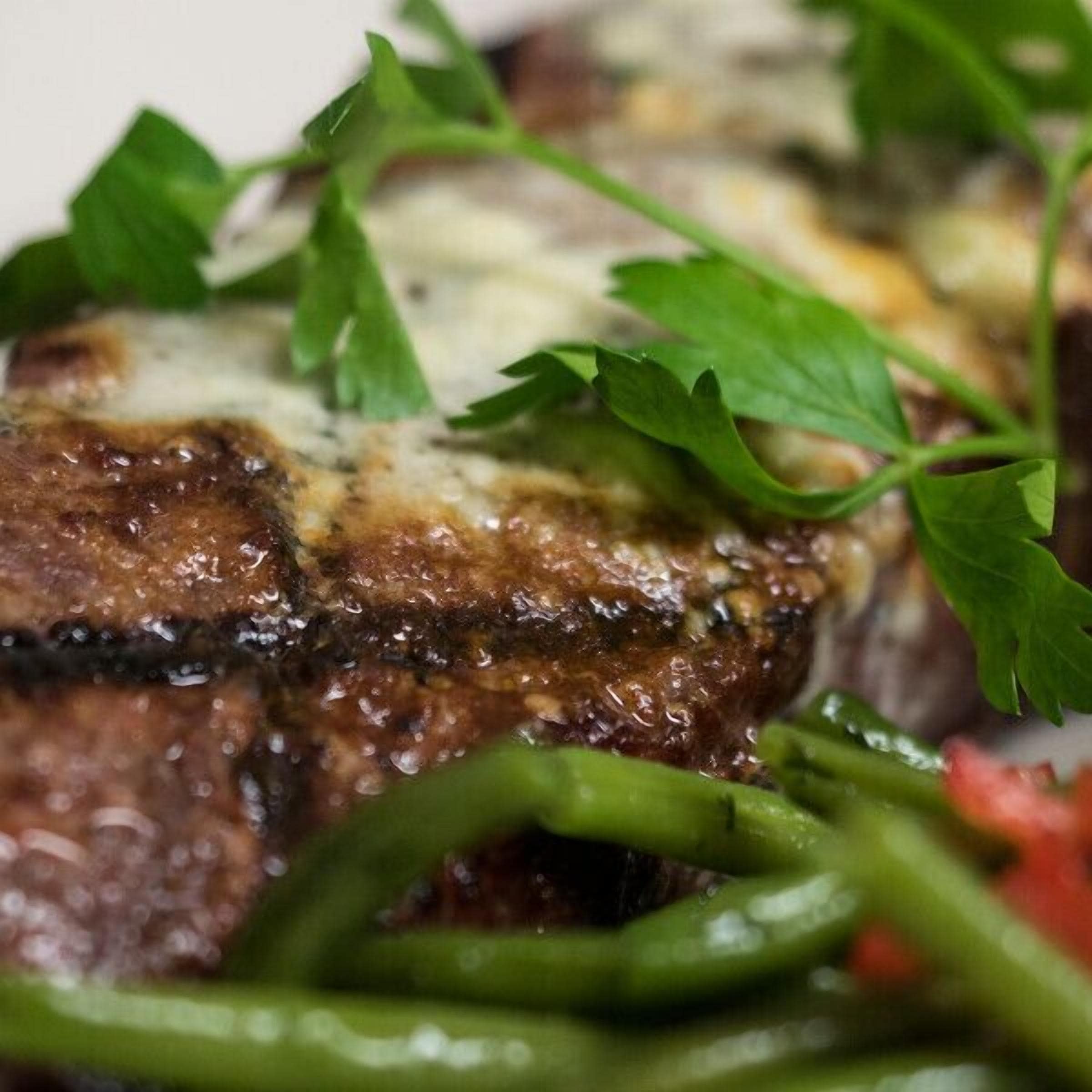 Une vue rapprochée d’un steak grillé, nappé de fromage fondu et garni d’herbes fraîches.