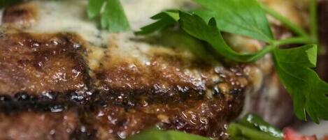 Une vue rapprochée d’un steak grillé, nappé de fromage fondu et garni d’herbes fraîches.