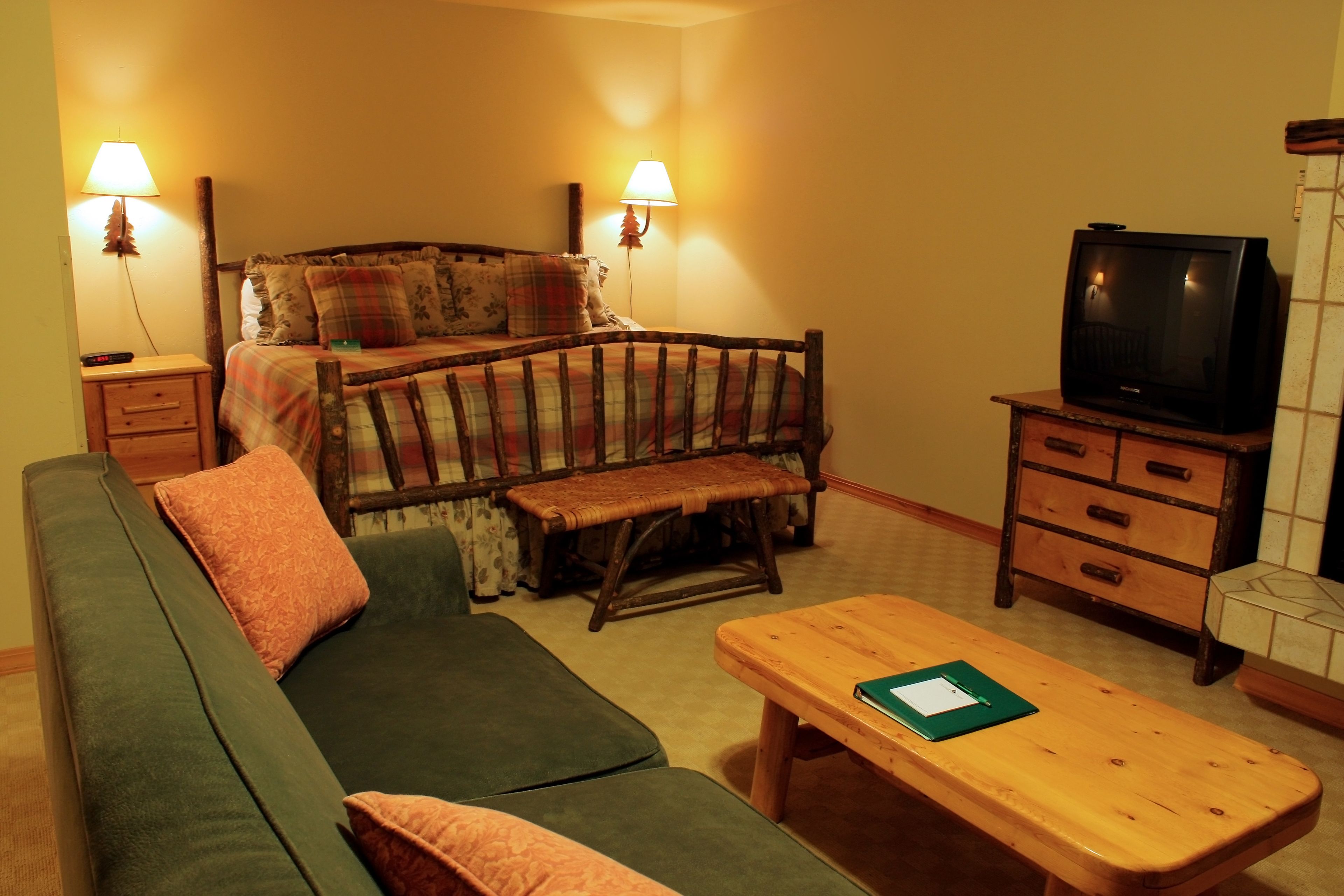 Una habitación acogedora con un sofá verde, un banco de madera, una mesa de madera, un televisor y dos lámparas.