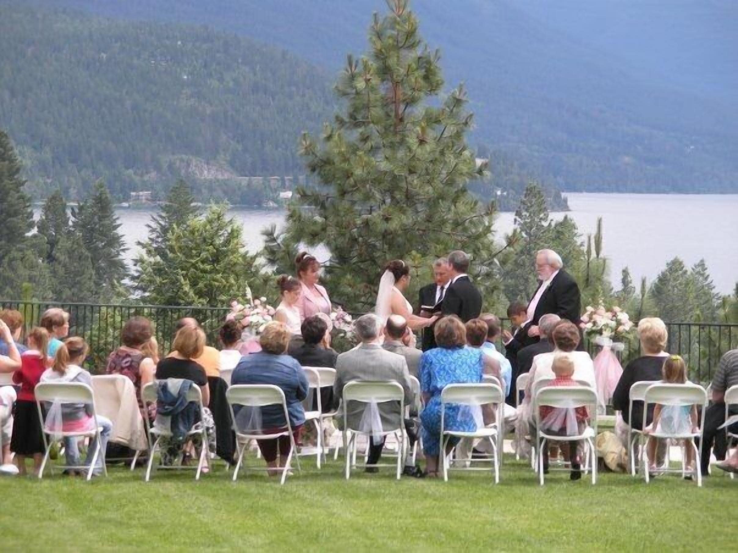 A wedding ceremony outdoors with guests seated on white chairs facing the ceremony area.